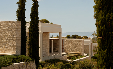 Deluxe pool pavilion at Amanzoe resort, featuring stone architecture and cypress trees framing the structure.