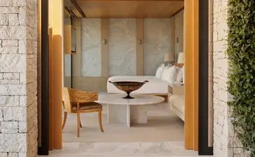 Pavilion bedroom at Amanzoe resort with stone walls, wooden doors, and minimalist furnishings.