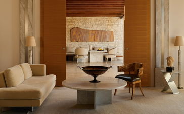 Pavilion accommodation interior at Amanzoe resort, with warm wooden walls, cream seating, and minimalist furnishings.