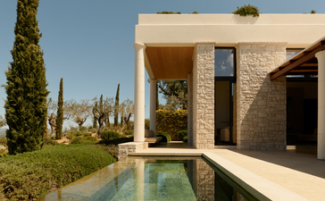 Infinity pool stretching alongside a modernist stone pavilion at Amanzoe, with cypress trees lining the Peloponnese landscape.