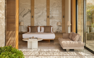 Chambre principale avec lit bas moderne, murs en pierre naturelle et baies vitrées chez Amanzoe.