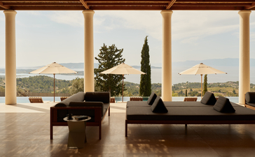 Villa 22 lounge at Amanzoe resort, with expansive windows framing Aegean views and cypress trees.