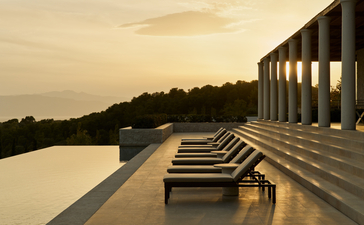 Villa terrace with sunloungers overlooking still water at dusk, Amanzoe resort.