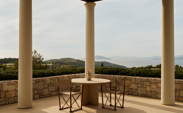Dining table and chairs on a stone terrace at Amanzoe, overlooking the Peloponnese countryside.