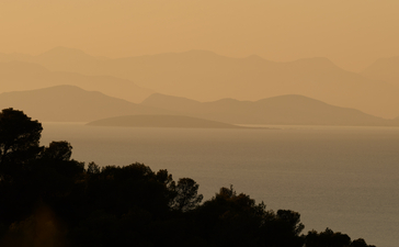 Silhouetted pine trees frame a misty coastal view at Amanzoe, with mountains softly visible across the water.