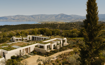 Whitewashed villa at Amanzoe set among pine trees with Aegean Sea and distant mountains visible beyond.