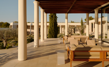 Villa terrace with wooden seating overlooking Amanzoe resort and distant coastline.