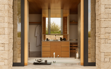 Villa entrance at Amanzoe resort, framed by stone columns with wooden doors opening onto a light-filled interior.