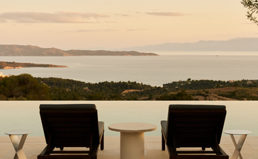 Two black chairs facing calm waters at Amanzoe at dusk, with distant coastline visible.