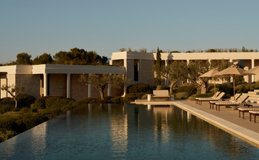 Amanzoe villa with reflecting pool at dawn, stone architecture set against clear sky.