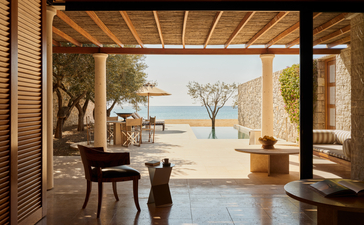 Beachside cabana at Amanzoe with open doors framing a sandy beach and sea view, featuring wooden ceiling and minimalist décor.