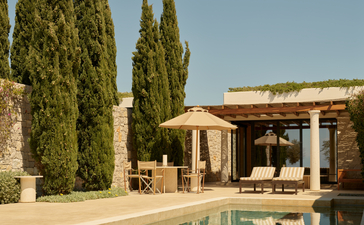 Beachside cabana with pergola overlooking the pool at Amanzoe, framed by cypress trees.
