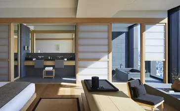 Bathroom and lounge area of an Aman Suite at Aman Tokyo hotel, featuring wooden panelling, modern fixtures, and floor-to-ceiling windows.