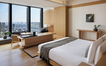 Aman Suite bedroom at Aman Tokyo with city views, bed, and workspace by floor-to-ceiling windows.