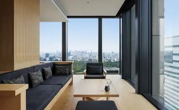 Aman Tokyo suite lounge dengan sofa biru, pemandangan kota Tokyo melalui jendela kaca besar.