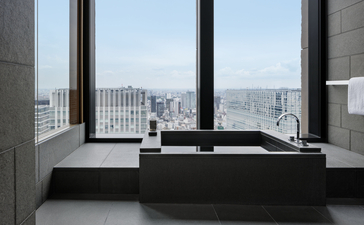Salle de bains de la City Suite à Aman Tokyo, avec baignoire noire et vue sur Tokyo.