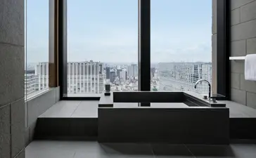 Spacious bathroom at Aman Tokyo with freestanding black bathtub positioned before floor-to-ceiling windows overlooking the city skyline.