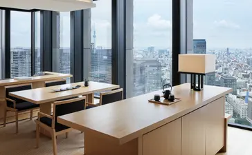 Dining area in Aman Tokyo city suite with wooden table, floor-to-ceiling windows overlooking Tokyo skyline.