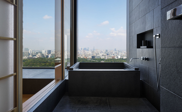 Deluxe suite bathroom at Aman Tokyo with freestanding soaking tub overlooking the city skyline.