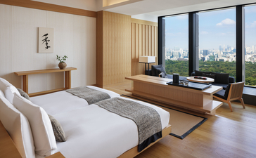 Deluxe suite bedroom at Aman Tokyo with wooden furnishings, white bedding, and floor-to-ceiling windows overlooking the city.