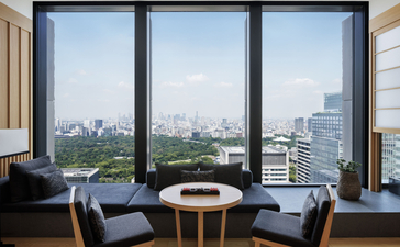 View of Tokyo skyline from Aman Tokyo deluxe suite bedroom with floor-to-ceiling windows and seating area.
