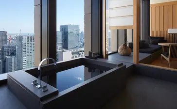 安缦东京酒店大套房，宽敞的浴室配深色浴缸，落地窗俯瞰东京城市景观。