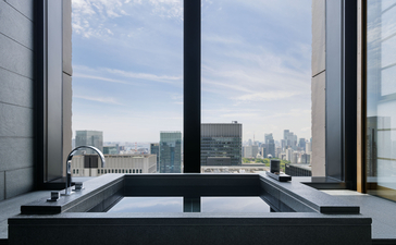 Salle de bains panoramique avec baignoire noire et vue sur Tokyo à l'Aman Tokyo.