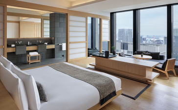 Panorama suite bedroom at Aman Tokyo with bed, seating area, and expansive city views through floor-to-ceiling windows.