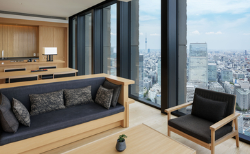 Vue panoramique depuis la suite lounge d'Aman Tokyo, avec canapé gris et vues étendues sur la ville.
