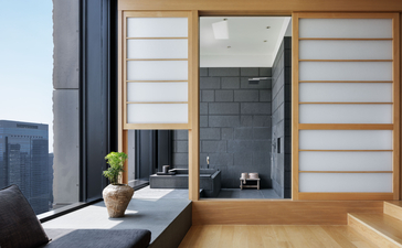 Aman Tokyo suite bathroom with soaking tub, slate wall, and adjoining lounge area with wooden screens.