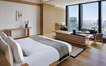 Spacious principal bedroom at Aman Tokyo hotel with floor-to-ceiling windows overlooking the city skyline, wooden furnishings, and serene minimalist design.