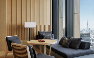 Tokyo Suite lounge at Aman Tokyo with wooden desk, chair, and floor-to-ceiling windows overlooking the city skyline.