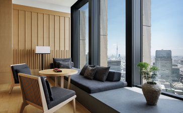 Tokyo Suite lounge at Aman Tokyo with floor-to-ceiling windows overlooking the city skyline, featuring wooden panelling and contemporary furnishings.