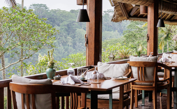 Dining pavilion at Amandari with wooden table and chairs overlooking verdant valley views.