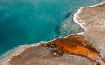 Aerial view of a geothermal hot spring with vivid orange and turquoise waters at Amangani, overlooking Yellowstone National Park.