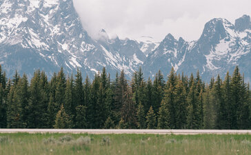 Amangani's exterior set against the Teton Mountains, with forested foothills and open meadow.