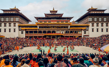 Festival celebration at Aman Bhutan, with colourful crowds gathered in a courtyard surrounded by traditional architecture.
