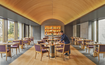 养云安缦度假村的餐厅内部，拱形天花板下摆放木质餐桌和椅子，两侧大窗採光。