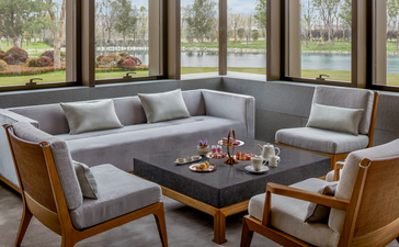 Bar lounge at Amanyangyun with grey sectional sofa, wooden armchairs, and dark coffee table overlooking gardens.