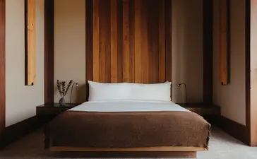Deluxe Suite bedroom at Amangani with wooden bed frame and white pillows in warm-toned interior.
