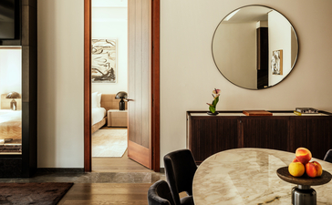 One-bedroom home at Aman New York with round mirror, marble vanity, and open doorway to adjoining room.