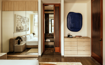 Bedroom at Aman New York with wooden cabinetry, light walls, and a seating area by the window.