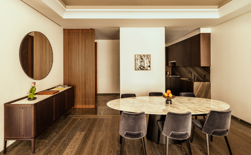 Dining area in a one-bedroom home at Aman New York, featuring a wooden table, upholstered chairs, and warm wood furnishings.