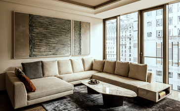 Living area in a one-bedroom home at Aman New York, featuring a light-colored sectional sofa and floor-to-ceiling windows overlooking the city.