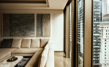 Living room in a one-bedroom home at Aman New York, with city views through floor-to-ceiling windows and neutral furnishings.