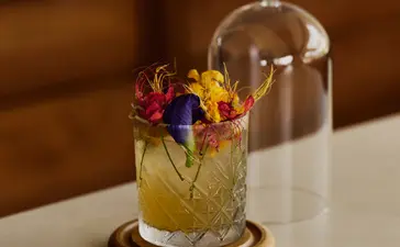 Cocktail under a glass dome with edible flowers at Amanera resort bar.