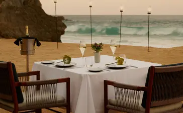 Dining table set on the beach at Amanera resort, with ocean views and coastal cliffs.