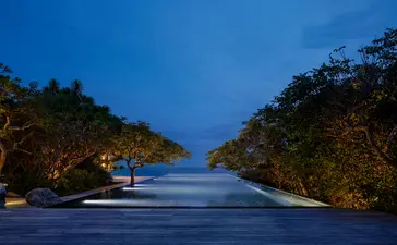 安缦诺怡度假村的三卧海景泳池住宅外观，夜幕下照明温暖，通往大海的步道蜿蜒其间。