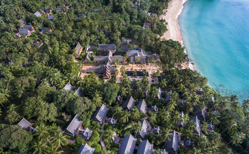 Aerial view of Amanpuri resort nestled amongst tropical forest along a turquoise beach in Thailand.