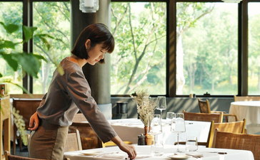 Staff member arranging dining table at Amanyangyun restaurant with garden views.